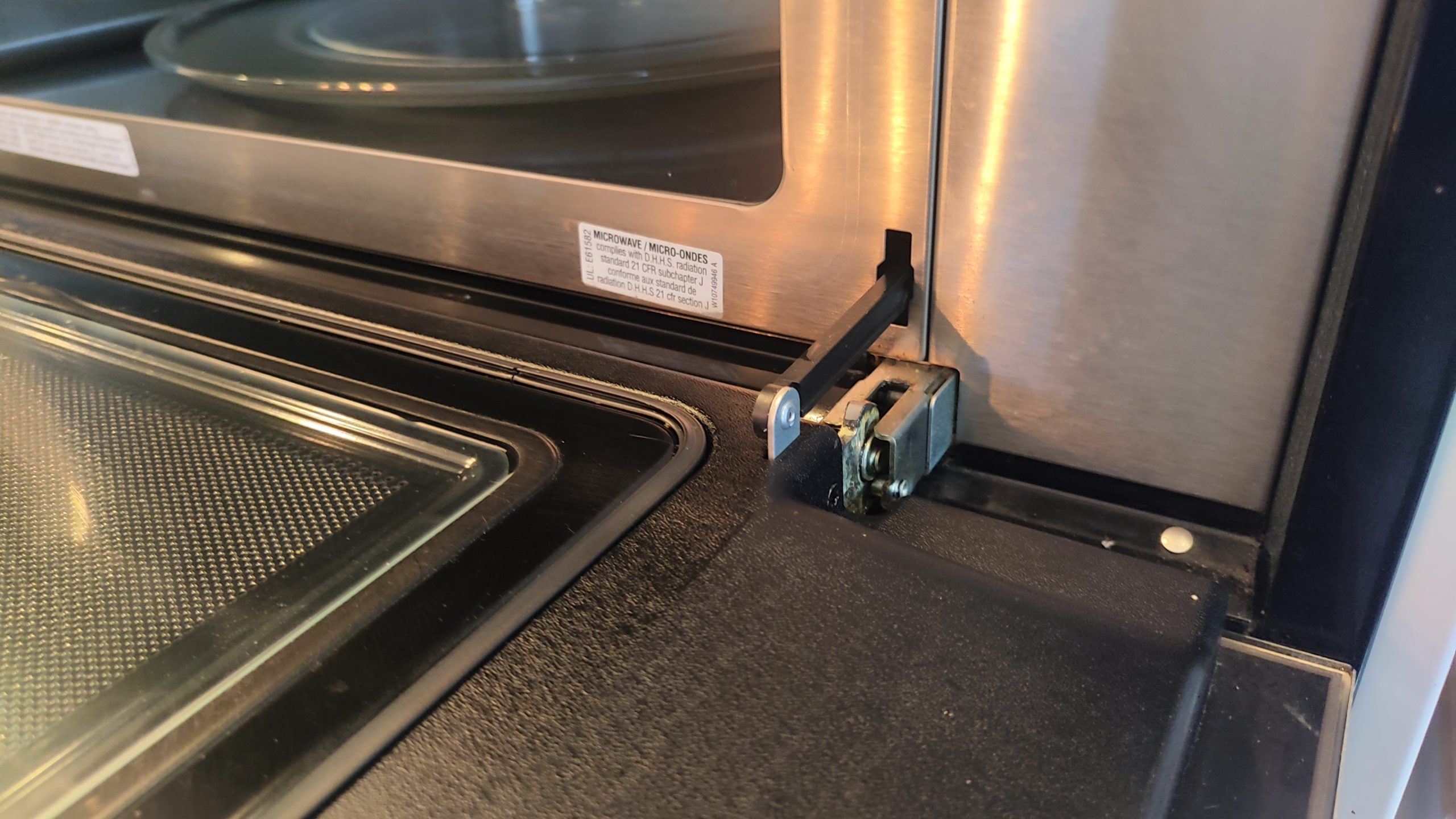 Close-up of the right microwave door hinge mechanism on a Whirlpool WOC97ES0ES02 before repair